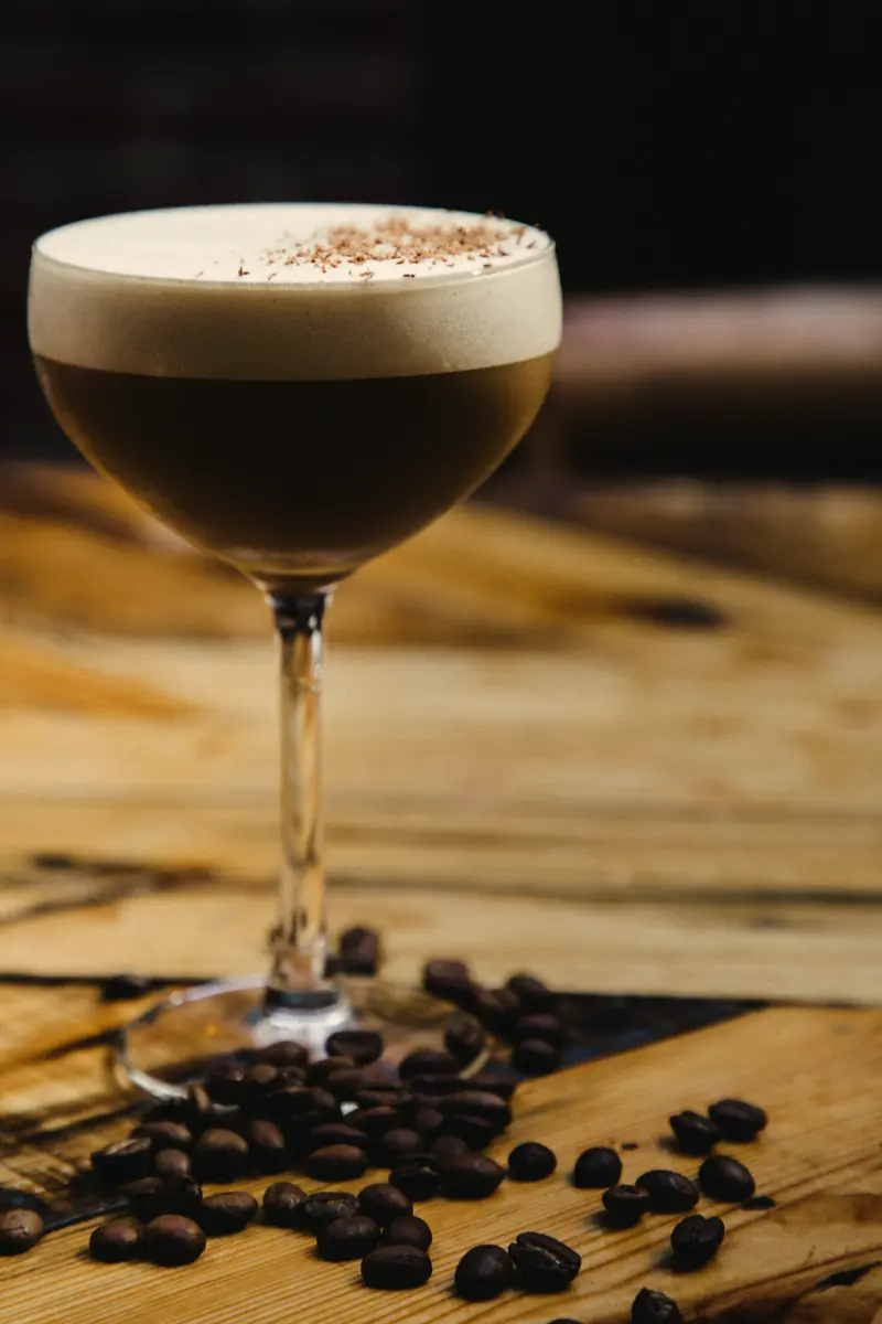 Espresso martini com espuma clara sobre mesa de madeira com grãos de café