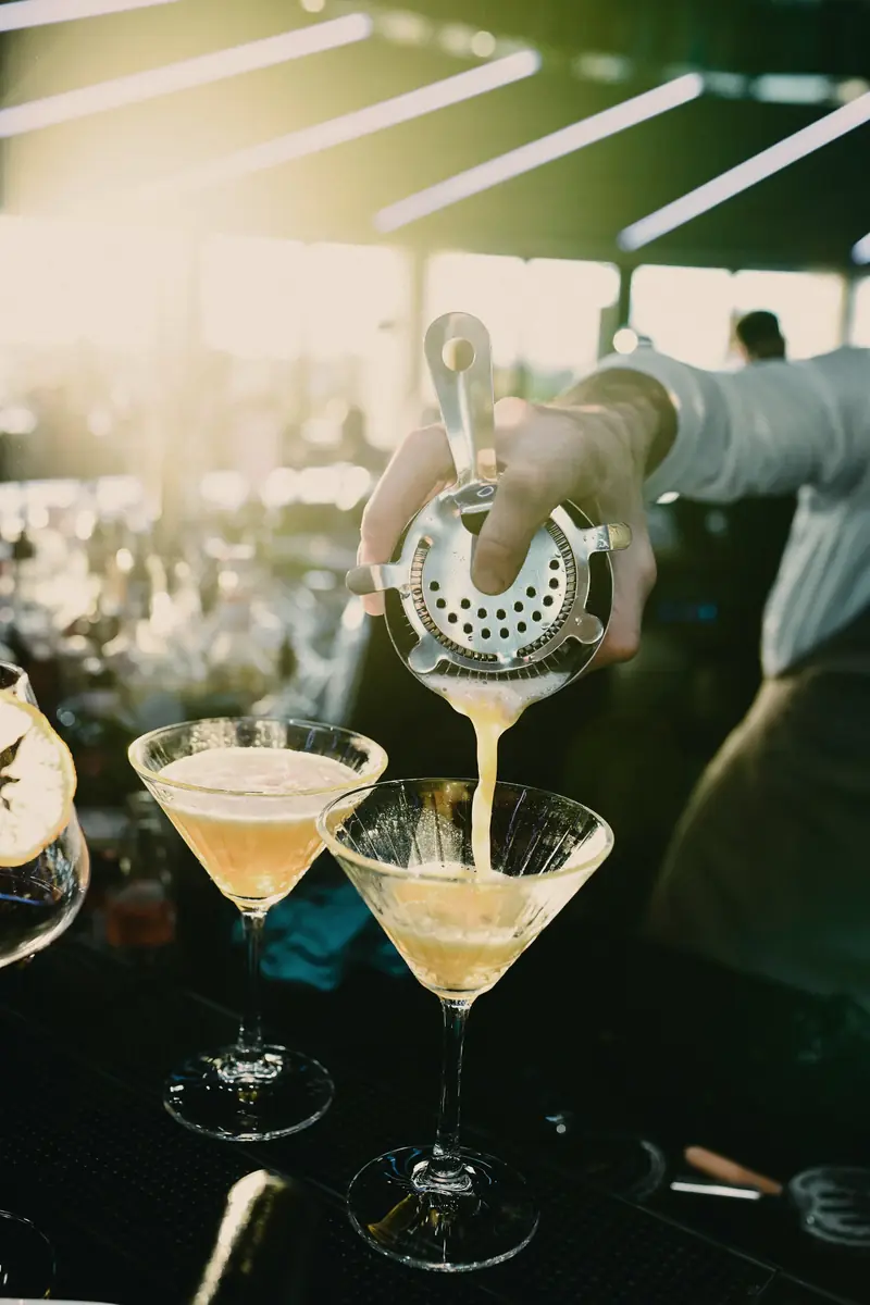 Bartender servindo dois drinks em taças martini durante um evento