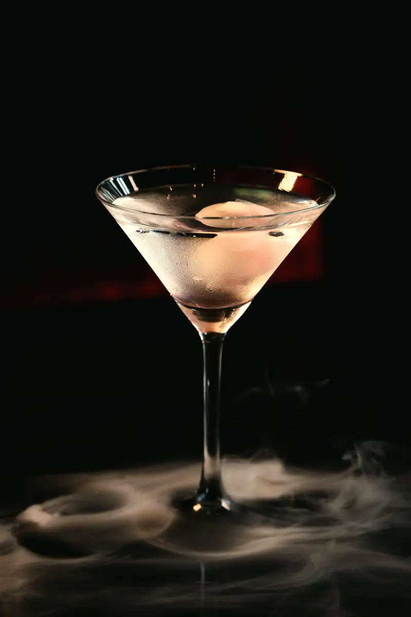 Taça martini sobre mesa escura com fumaça ao redor da base