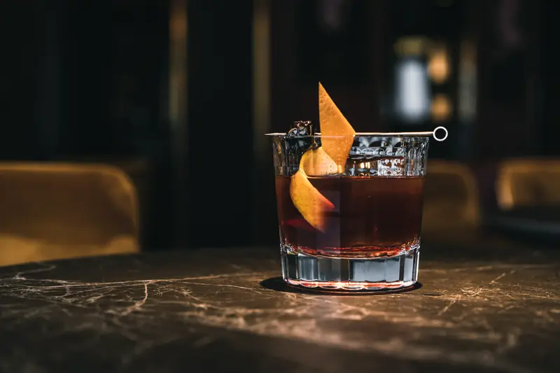 Drink em copo baixo com casca de laranja sobre mesa de mármore