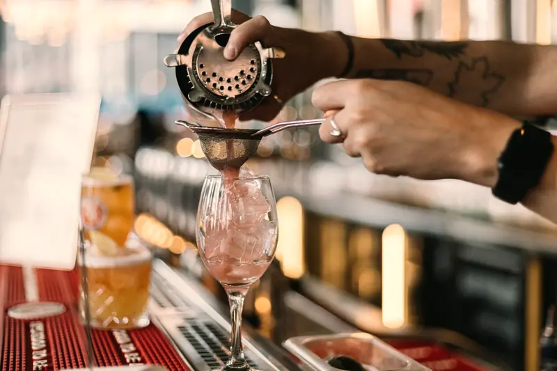 Mãos de bartender coando um drink no balcão de um bar movimentado