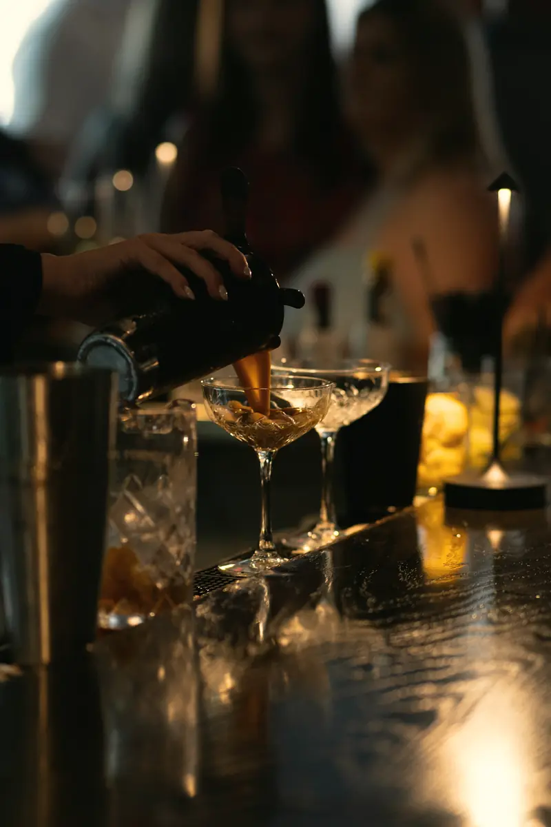 Bartender servindo drinks em taças coupe sobre o balcão, à luz de velas